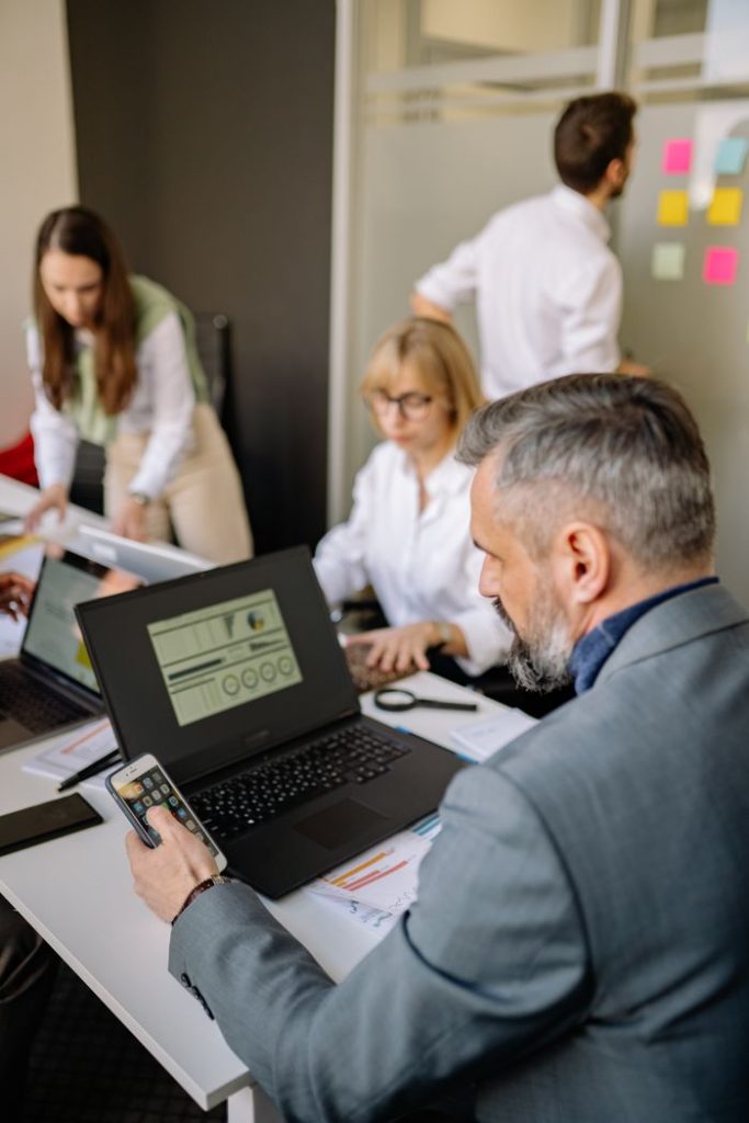 a-man-using-his-smartphone-in-the-office-7793166 Corporate team working together with technology in a modern office setting, promoting collaboration and productivity.