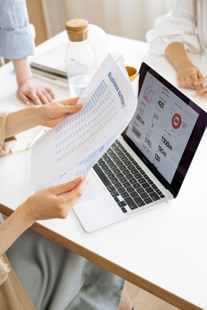 person-holding-a-paper-8512441 Modern office setting with a business report and laptop display on a white desk.